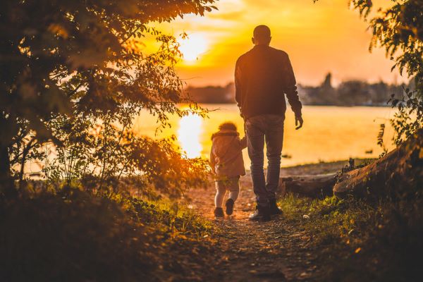 Man and little girl walking hand in hand in front of sunset