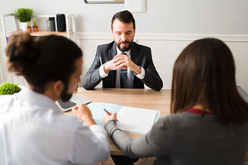 A bearded man faces a young couple signing a mediation agreement after they’ve engaged in divorce mediation.