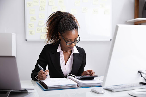 A young, Black, female forensic accountant reviews financial records with a calculator. Forensic accountants can uncover hidden assets in divorce proceedings.