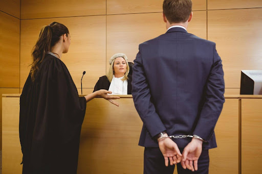 A man in handcuffs standing before a judge facing felony charges.