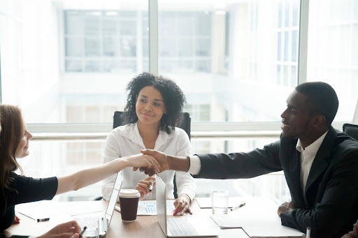 A smiling mediator sits between two spouses, shaking hands after coming to an agreement during a mandatory mediation session.
