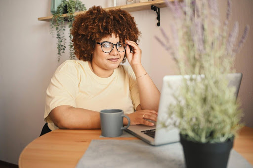A woman sitting at a small table in a domestic setting with a cup of coffee and an open laptop computer, preparing for virtual mediation in divorce.