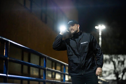 An officer in a black jacket with a flashlight moments before a security guard assault.